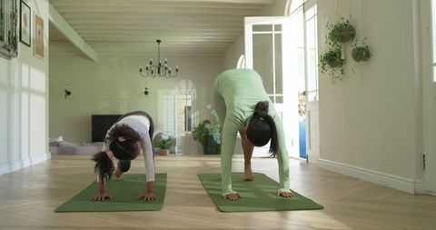 Woman and girl practicing yoga together folding into forward bend on green mats at home