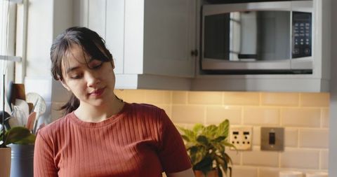 Asian woman in bright kitchen with utensils and tile backsplash