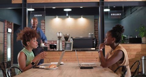 African colleagues collaborating over laptops at wooden cafe table, discussing work ideas