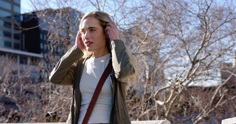 Young woman adjusting over-ear headphones on urban balcony during sunlit city commute