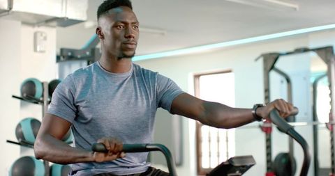 African american man pedaling on exercise bike wearing fitness tracker in bright gym