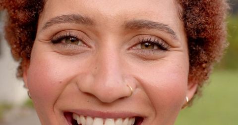 Smiling woman with curly hair and nose ring in garden