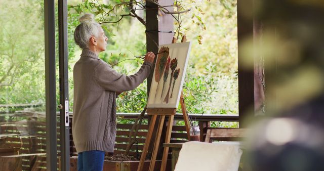 Senior woman painting on canvas using easel outdoors in beautiful garden. Useful for content related to retirement hobbies, creative pursuits, senior activities, leisure, and outdoor painting. Ideal for blogs, websites, and articles focused on art therapy, senior wellbeing, and natural inspiration for artists.