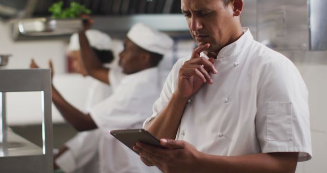 Biracial male chef using tablet in restaurant kitchen. Working in a busy restaurant kitchen.
