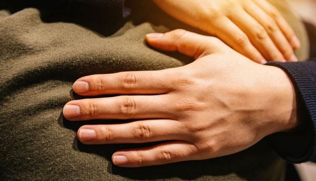 Resting hands conveying comfort and intimacy on olive-green knit with dark sleeve cuff