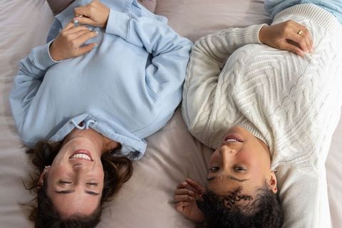 Female friends lying on bed sharing relaxed conversation and cozy intimate bedroom lifestyle
