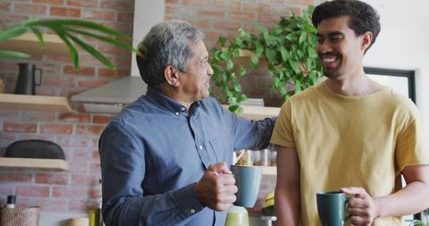 Sharing morning coffee between senior father and adult son in bright home kitchen