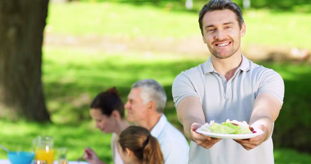 Cheerful Man Showing Plate of Food at Outdoor Family Picnic - Download Free Stock Images Pikwizard.com