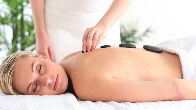 A serene scene of a woman experiencing a hot stone massage at a spa. Her facial expression conveys relaxation and contentment, offering a glimpse into a luxurious wellness experience. This is ideal for use in health and wellness promotions, spa advertisements, or self-care blogs, showcasing the benefits of spa treatments and relaxation therapies.