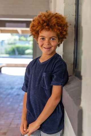 Smiling boy leaning on porch ledge wearing navy t-shirt and casual summer outfit