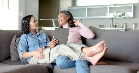 Friends Laughing and Relaxing on Sofa with Tablet in Modern Living Room