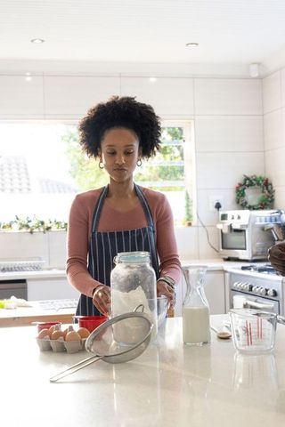 African american woman preparing baking ingredients at bright kitchen island with flour