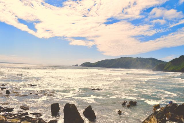 This image showcases a scenic ocean view with a rocky shoreline and distant hills under a partly cloudy sky. Ideal for use in travel guides, nature blogs, and coastal tourism promotions.