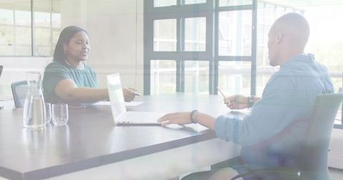 Exchanging business card across modern conference table with laptop during daytime meeting