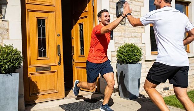 Runner exiting home celebrating finish with high-five outside suburban doorstep, smiling