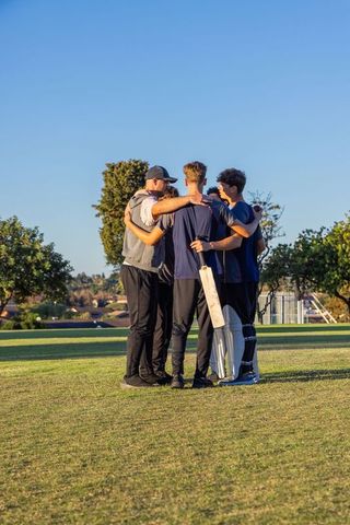 Cricket team huddling on sunlit field holding bat and pads before match