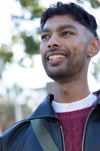 Young indian man smiling outdoors in black leather jacket and maroon sweater portrait