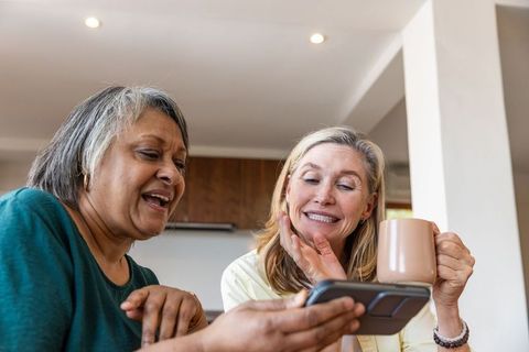Senior Friends Enjoying Coffee and Smartphone Together in Kitchen