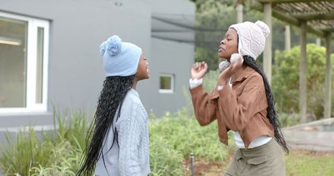 Two african american girls laughing and playing candidly in yard wearing knit beanies