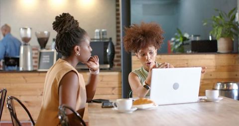 Collaborating over laptop in cafe, woman pointing and explaining to colleague during meeting