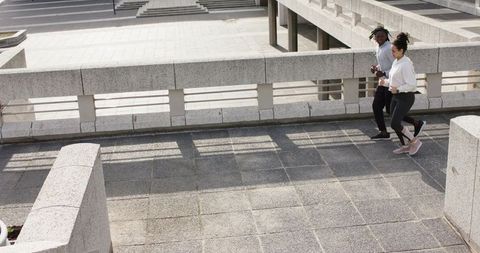 Diverse friends jogging side by side on urban elevated concrete plaza walkway, sunlit