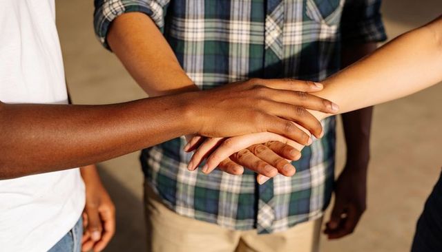 Diverse team stacking hands showing teamwork and unity overlapping forearms closeup
