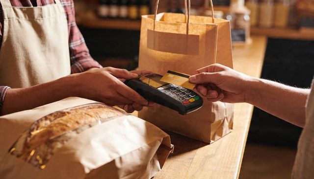 Customer tapping card on contactless terminal at rustic bakery counter with wrapped loaf