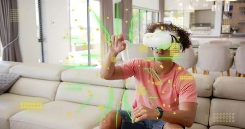 Young man wearing white VR headset interacting with green AR holograms in living room