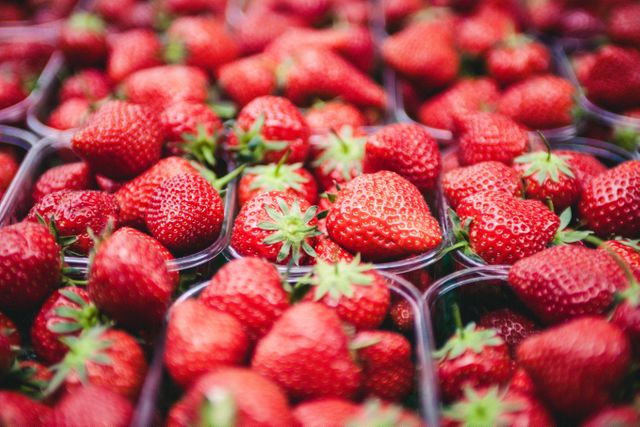 Bright red strawberries fill multiple plastic containers, highlighting their freshness and appealing texture. Suitable for advertising healthy eating, organic produce, and summer fruit promotions. Can be used in food blogs, recipes, grocery store ads, and nutritional articles.