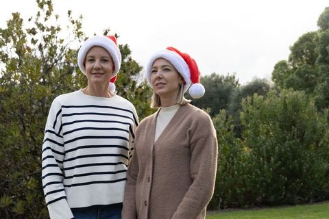 Middle-aged women in santa hats standing in backyard celebrating relaxed outdoor christmas