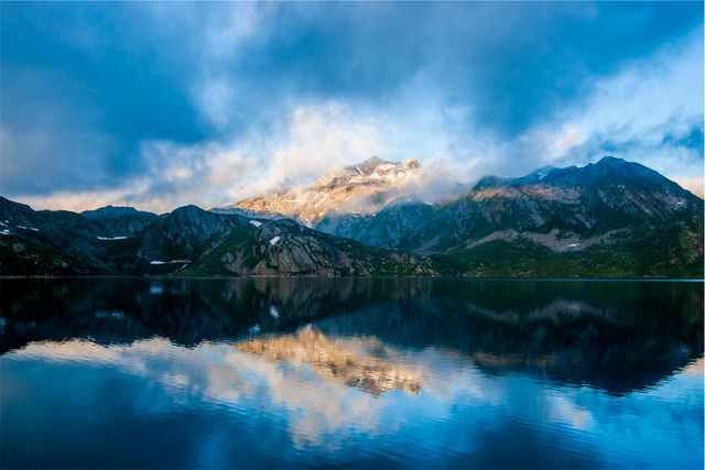 Tranquility prevails in this serene landscape featuring misty mountains reflecting in a lake at sunrise. Ideal for travel blogs, nature photography collections, relaxation features, and wilderness retreat promotions.