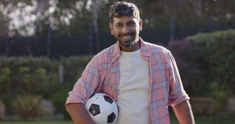 Smiling man holding soccer ball on sunny day