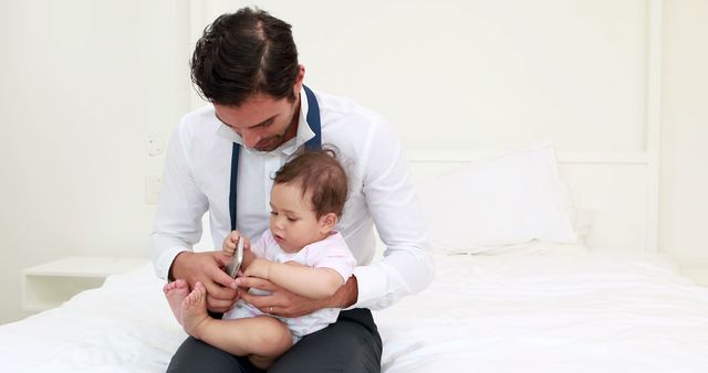 Cute baby grabbing her fathers smartphone on the bed