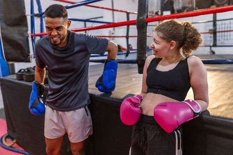 Boxing coach and teen girl sharing laughs while leaning on ring apron during training