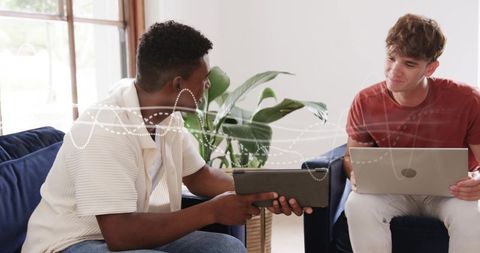 Two young men collaborating with tablet and laptop in bright home workspace