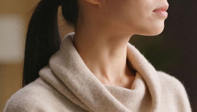Adult asian woman wearing beige cowl-neck sweater showing neckline and profile, soft light