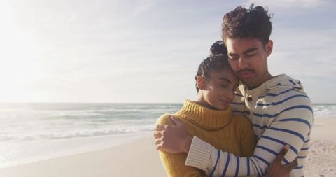 Hispanic couple embracing on sunlit beach
