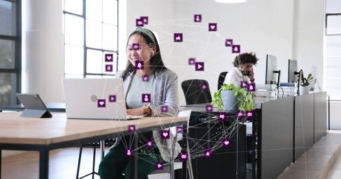 Asian woman working on laptop in modern open-plan office with digital network overlay