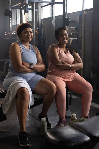 African american women sharing post-workout smile on gym bench, strength training break