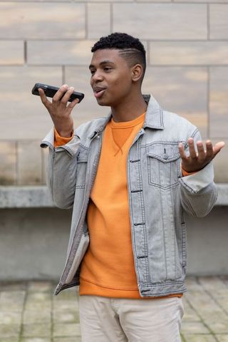 African american teen speaking into smartphone wearing orange sweatshirt and denim jacket outdoors