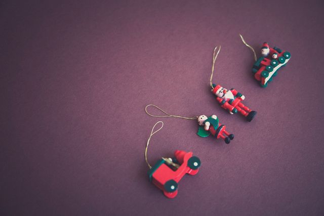 This composition features traditional wooden Christmas ornaments displayed against a solid purple background. These items exude a nostalgic holiday charm with their vibrant red and green colors. Ideal for usage in holiday marketing materials, festive greeting cards, seasonal blog posts, or any project aiming to capture the warm, cozy vibe of Christmas.