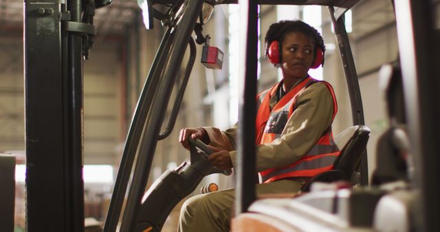 African american female worker wearing safety suit and sitting in turret truck in warehouse. global business, shipping and delivery.