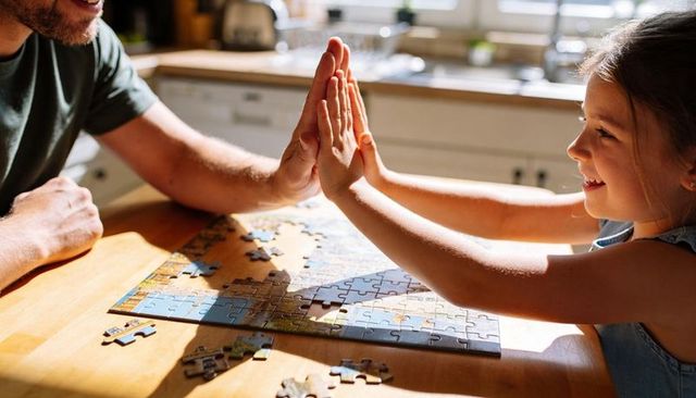 Father and daughter highfiving while finishing jigsaw puzzle on sunlit kitchen table