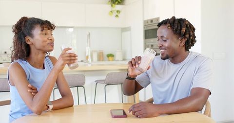 Young couple drinking smoothies at modern bright kitchen table, smiling, chatting and relaxing