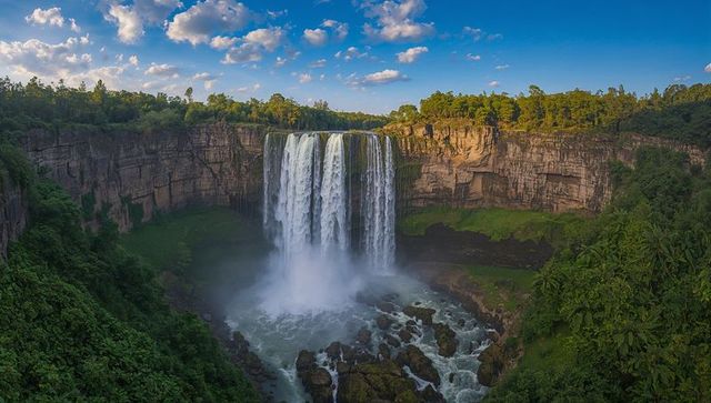 Cascading multi-stream waterfall plunging into river gorge with towering cliffs and mist