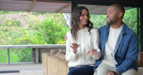 Smiling diverse couple sharing cozy moment on covered patio with lush garden greenery
