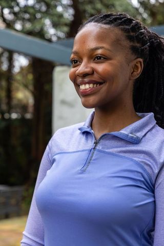 African american woman smiling in park wearing purple athletic quarter-zip top