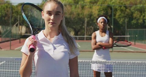Competitive women tennis players standing on court wearing white outfits holding rackets