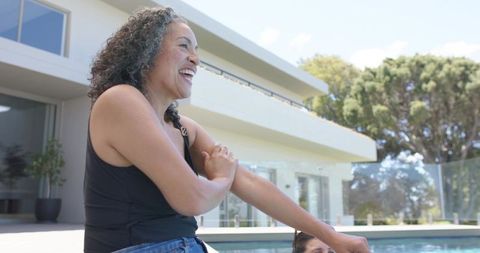 Laughing middle-aged woman relaxing at modern poolside by glass fence, summer lifestyle