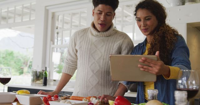 Image of happy biracial couple preparing meal together and using tablet. Domestic lifestyle and leisure time at home.